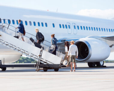 Outdoor shot of passengers boarding a flight, going up the steps to the airplane.