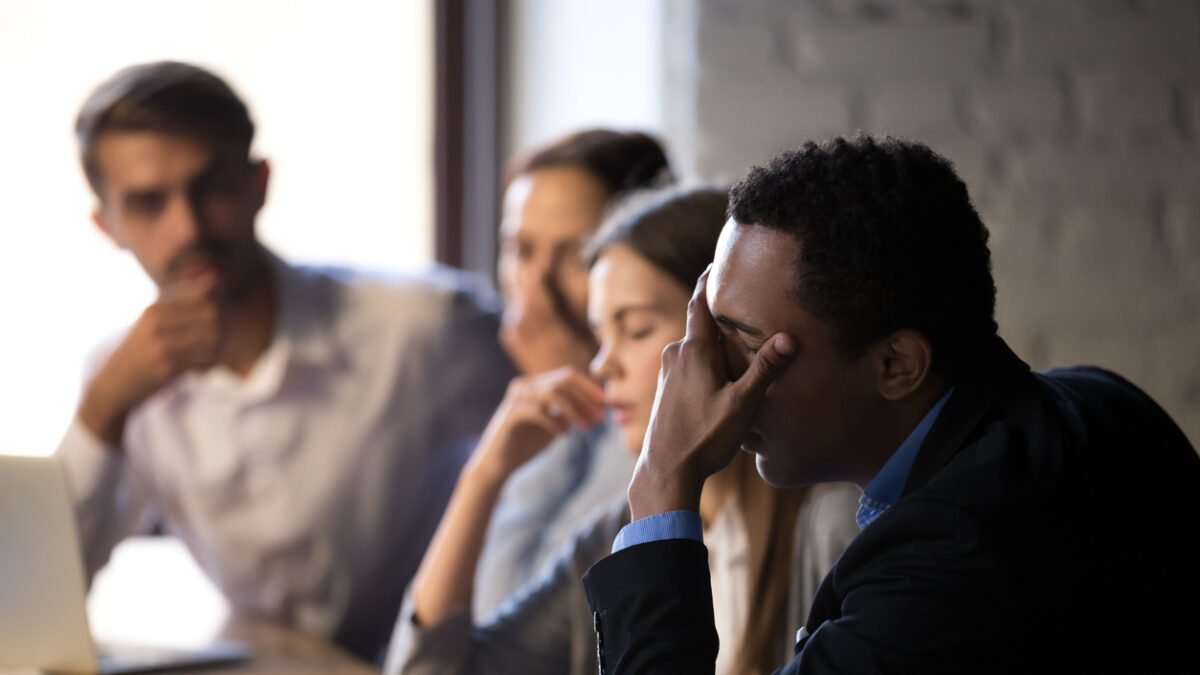 Disappointed diverse workers sit at office table, feel down reading bad company news online, depressed employees witness market bankruptcy or lose deal with customer, stressed colleagues have problem