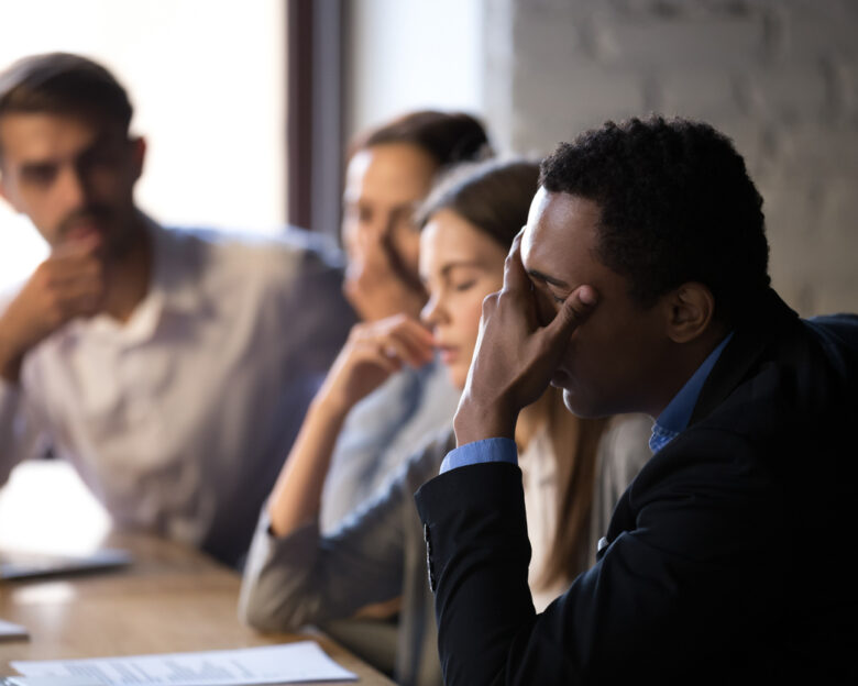 Disappointed diverse workers sit at office table, feel down reading bad company news online, depressed employees witness market bankruptcy or lose deal with customer, stressed colleagues have problem