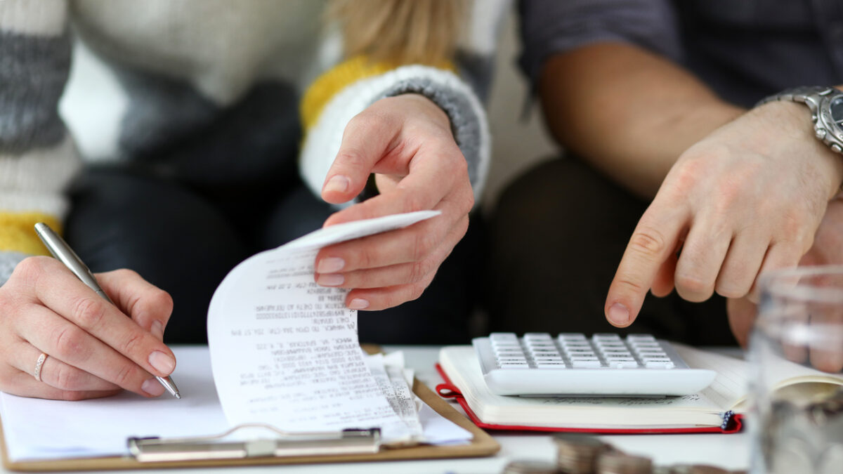 Close-up view of man and woman making account of family income. Writing down and calculating expenses. Attentive review of finance. Calculator on desk. Economy concept