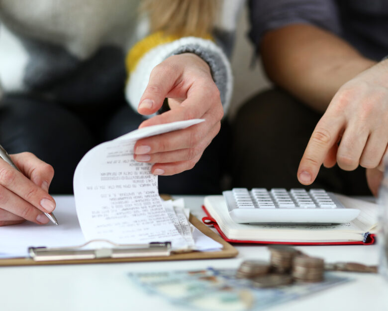 Close-up view of man and woman making account of family income. Writing down and calculating expenses. Attentive review of finance. Calculator on desk. Economy concept