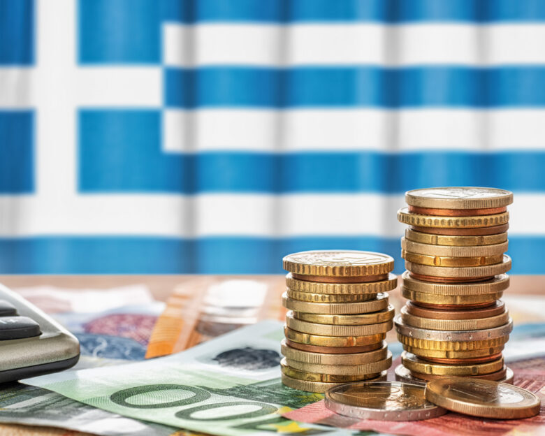 Euro banknotes and coins in front of the national flag of Greece