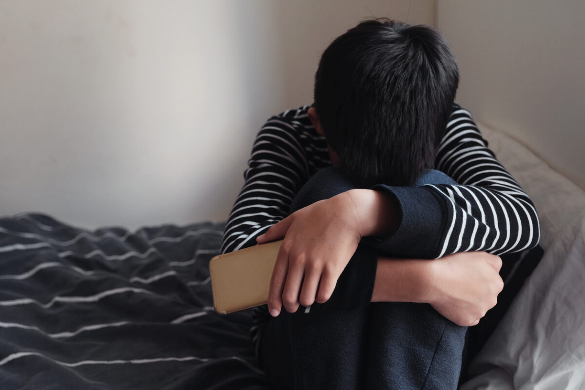 oung Asian preteen teenager boy hugging his knee in his bedroom with smartphone, Cyber bullying in kid, depressed child mental health