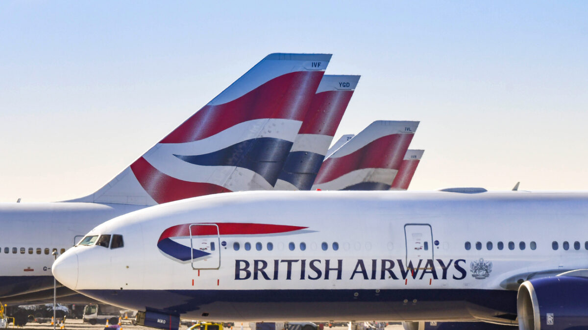 Boeing 777 long haul airliner operated by British Airways taxiing for take off past tail fins of the company's other aircraft