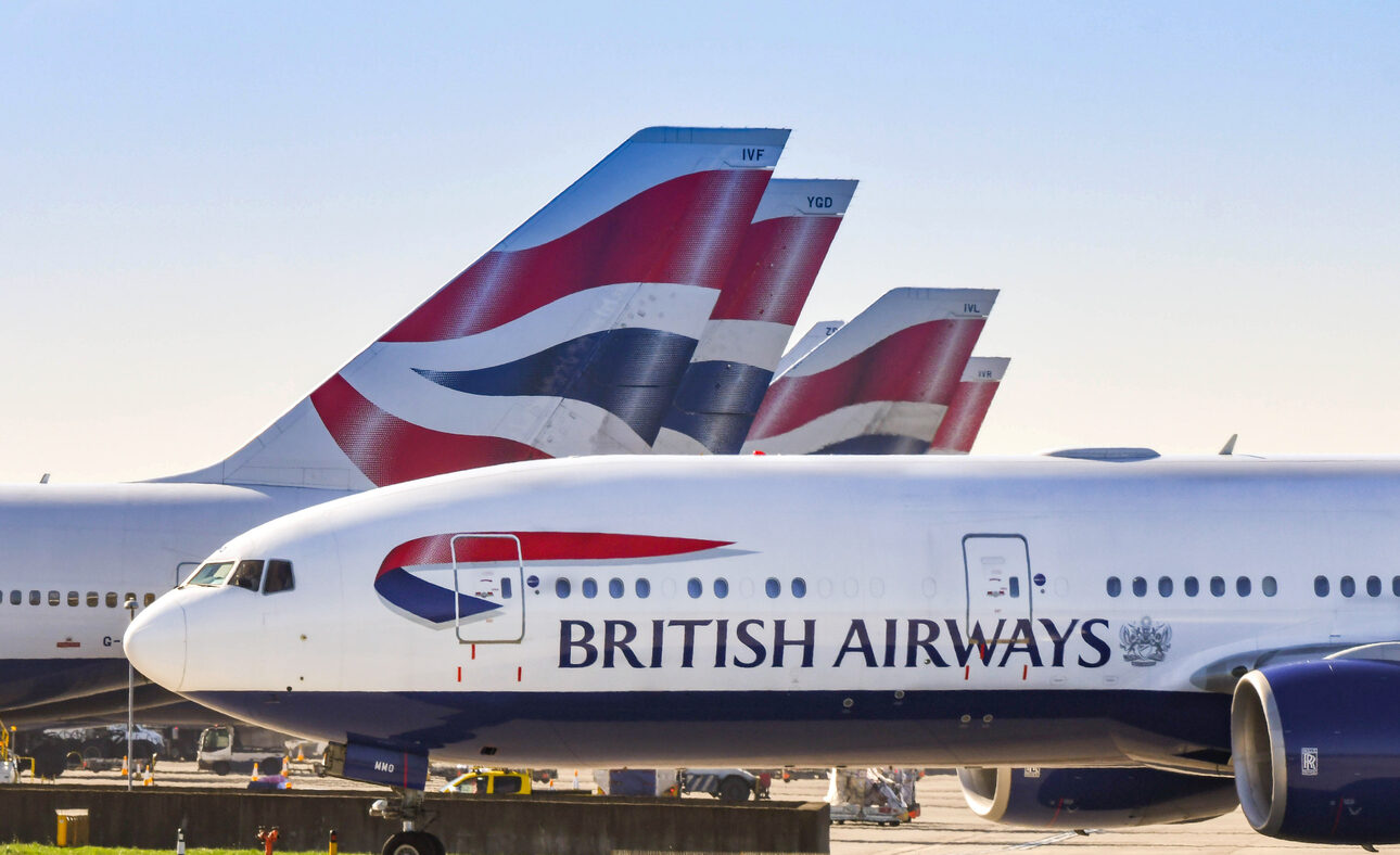 Boeing 777 long haul airliner operated by British Airways taxiing for take off past tail fins of the company's other aircraft