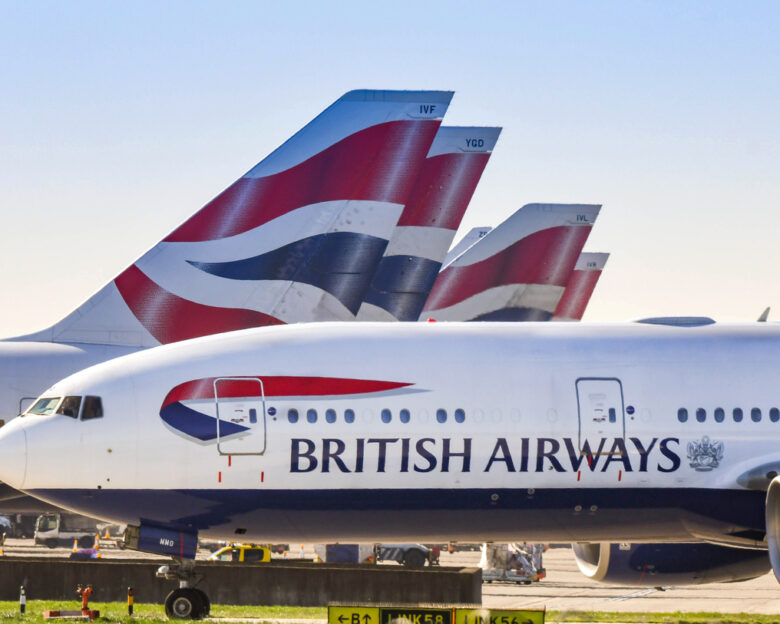 Boeing 777 long haul airliner operated by British Airways taxiing for take off past tail fins of the company's other aircraft