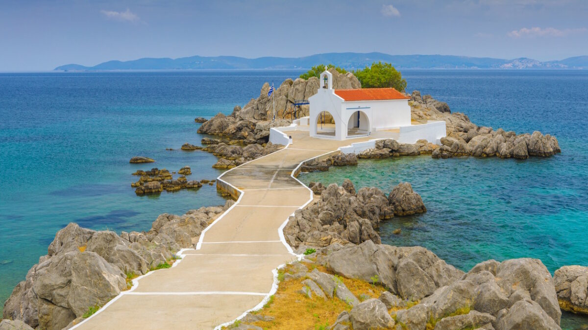 classical white greek church on a small rocky island in Agios Isidoros, Greece
