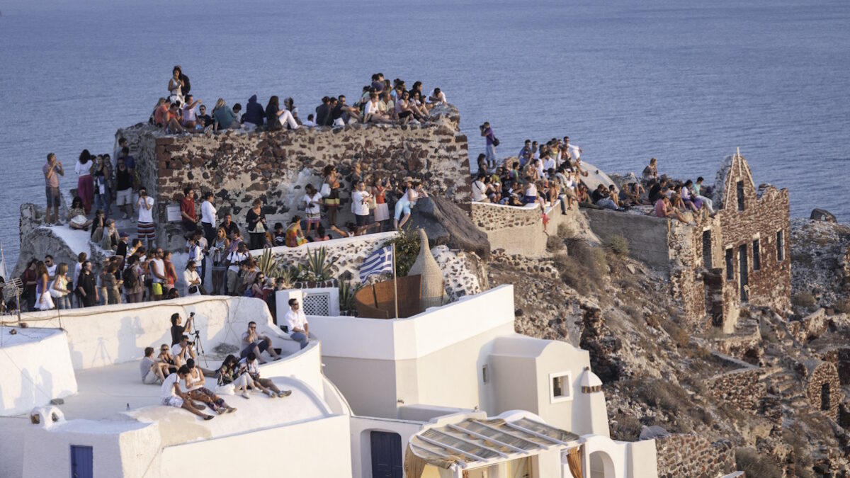 Oia,Santorini,Greece View of the Castle on the caldera of Oia in Santorini. Crowds of people perched on the half-ruined Castle and on the roofs of houses, waiting for the famous sunset.