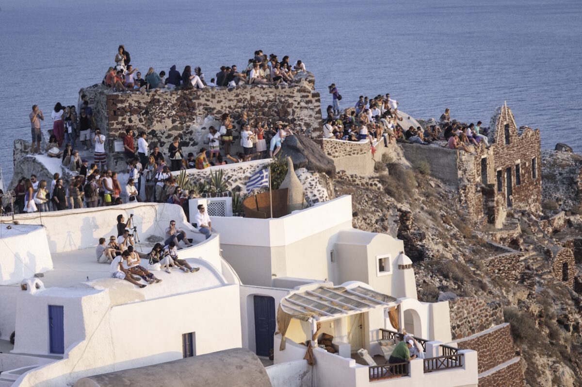 Oia,Santorini,Greece View of the Castle on the caldera of Oia in Santorini. Crowds of people perched on the half-ruined Castle and on the roofs of houses, waiting for the famous sunset.