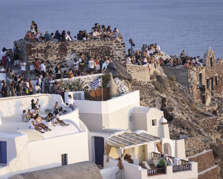Oia,Santorini,Greece View of the Castle on the caldera of Oia in Santorini. Crowds of people perched on the half-ruined Castle and on the roofs of houses, waiting for the famous sunset.