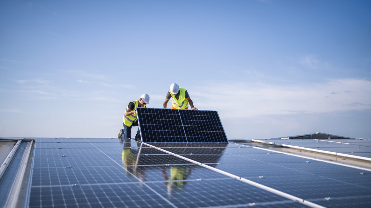 Team of two engineers installing solar panels on industrial factory roof.