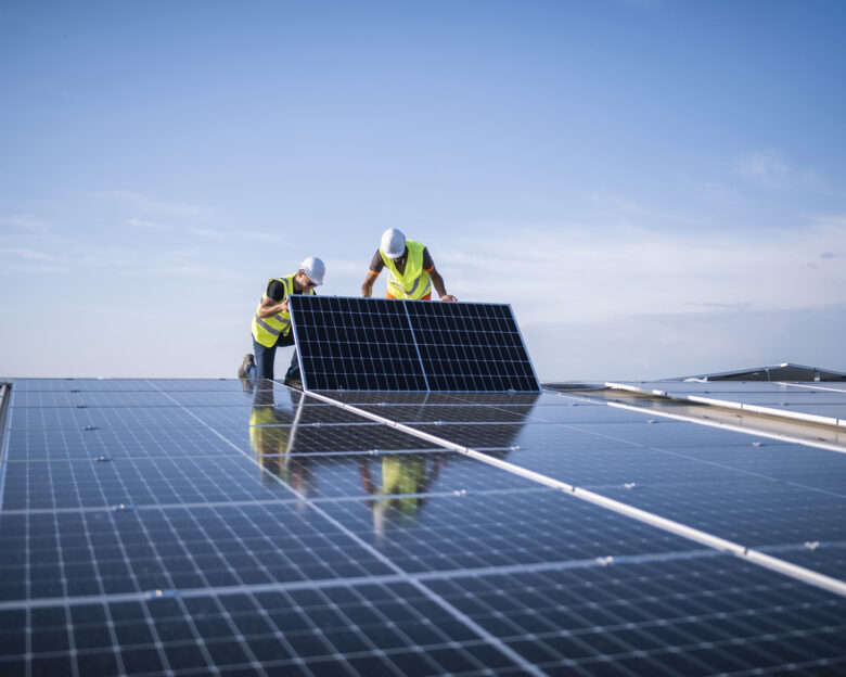 Team of two engineers installing solar panels on industrial factory roof.