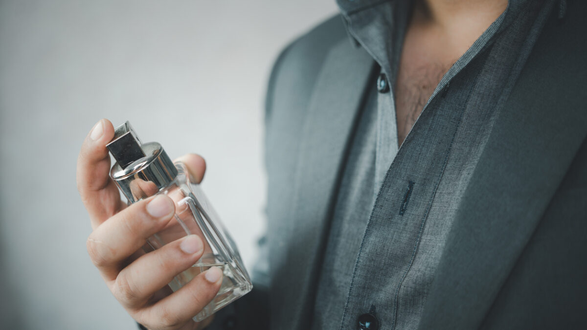 Handsome man in suit using perfume. Perfume bottle and spraying fragrance in hand