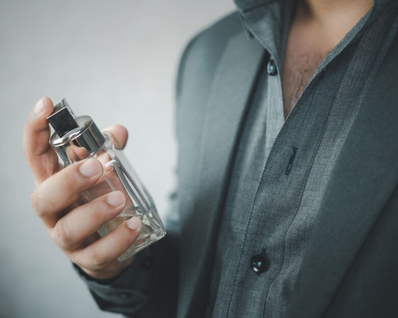 Handsome man in suit using perfume. Perfume bottle and spraying fragrance in hand