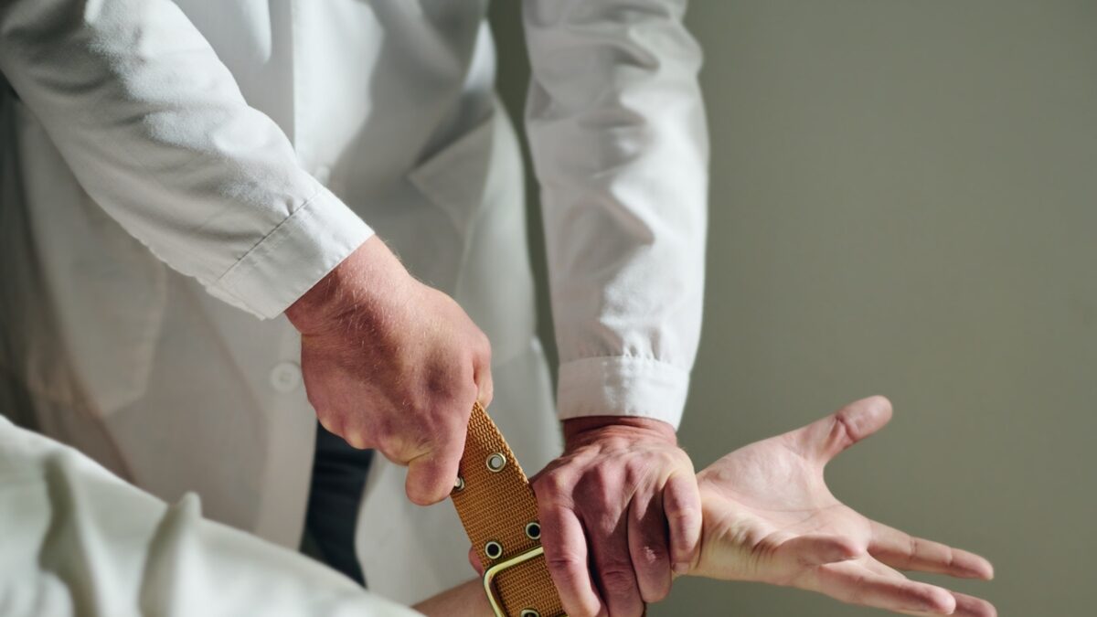 Close-up of male psychiatrist in lab coat binding hand of insane patient with belt to bed during seizure while trying to calm him down SSUCv3H4sIAAAAAAAACnRTTY/bIBC9V+p/iDgvKvgrZo+tVPVSqfdVDwOMY7QEIoO3ilb73wt2nCWr7MmeN7w3369fv+x2REIwijzuXrOVbGPtHOIE0XiXYPZwwSd0GqcSeZnqjpUAmNJCbaKfDNgSlBDV6OCICXSztRl+W5wkRIhzwJBzuUAKIh6SxgpeJdaEn1Z7tzkWZ2IkF/mD/mSRPBSeMMvs+Y2ObOga5ROJ7whzPH/7CWHMnbgnZYJCa8Ghn8O76Prz99qUAzp1fs8/88c5RpxC9Oq5LCS59jeBquoqu+llRe0l3iNzVrXtPYaeEI4hmqXtJUNUN/Fafo8tzWGJdhp99B8EfiHYON6I/PBO4SnOafD3krdwPH/MAiteNbCnleCKNj2rqFBc0oapQYqub0DomxC16rq+B0mHvUoENTDadx1SwXnyYMXkwN6Drz/LXC57NaFFWFftac2NPP9LEzmWywezNr7YuxevwOYHdaF0mowy7lDQfByXM9loys8uTrlkstVArPcnkGlBH3dD0sQNHyGE9FxveBFIpaP0xyKO83Ep4KJKdLqVbPK6rnnXNm368KYTPbs8WO9rNElnSWcTWmZrdFm6yRkQxdmgZcvpXjBBG9RAoekbWrU9Exp6gR2mLr/9BwAA//8DAKy92DJIBAAA