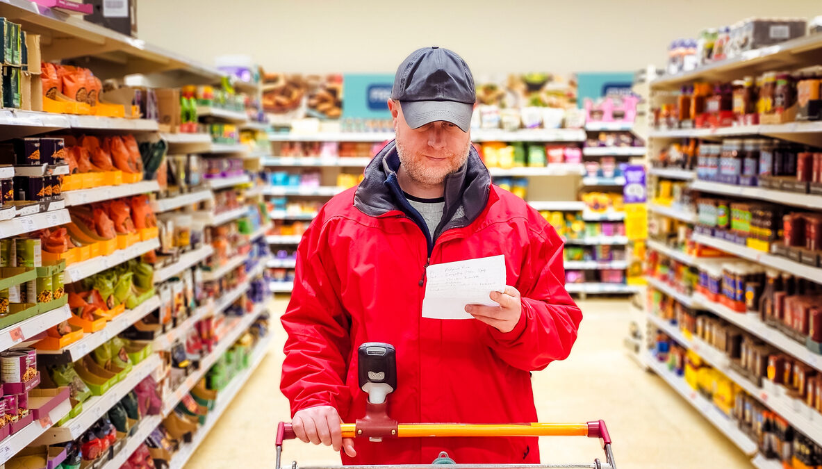 Mid adult man checking shopping list in supermarket aisle