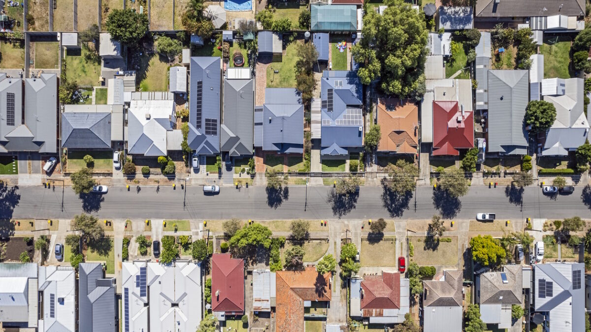 Aerial view directly above established houses in older Adelaide southern suburb: looking down on front & back yards some landscaped, one with construction work. Yellow & red topped wheeled garbage (rubbish) bins are parked on kerbside awaiting collection. Powerlines run down the street for the houses. Cars parked on the street and in private properties.