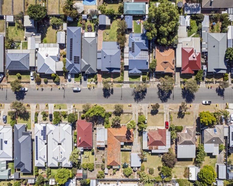Aerial view directly above established houses in older Adelaide southern suburb: looking down on front & back yards some landscaped, one with construction work. Yellow & red topped wheeled garbage (rubbish) bins are parked on kerbside awaiting collection. Powerlines run down the street for the houses. Cars parked on the street and in private properties.