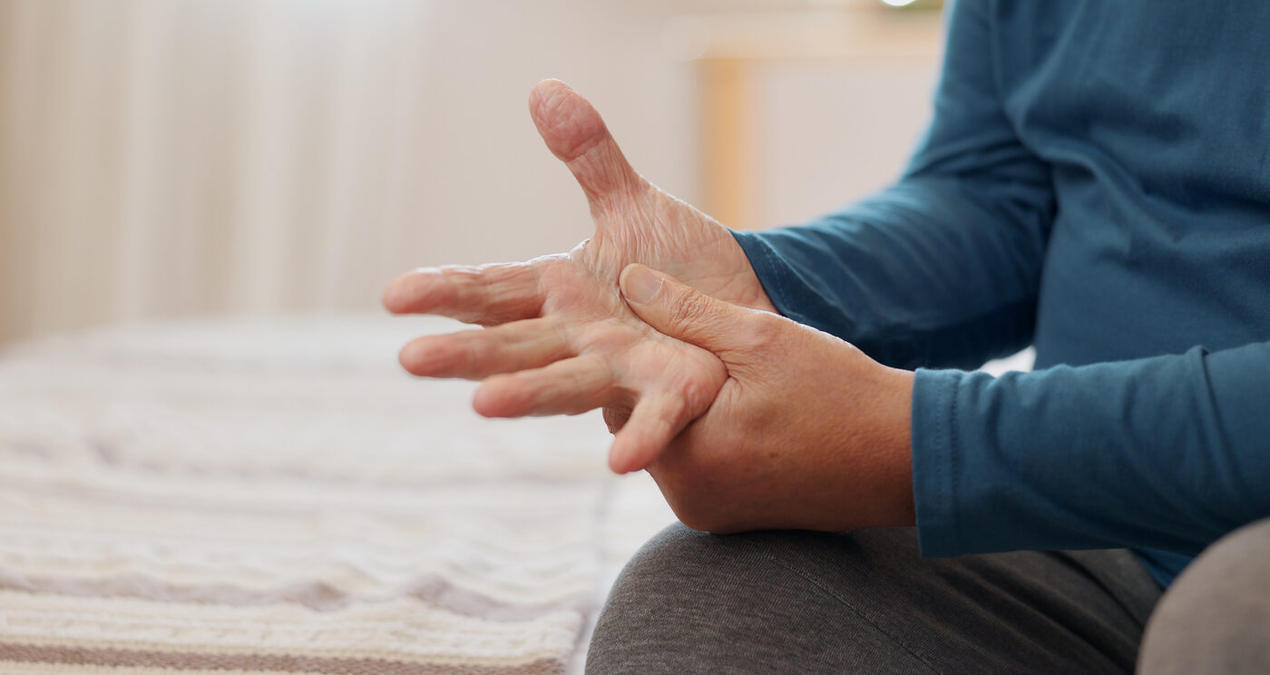 Senior man, hands and arthritis with joint pain, inflammation or Parkinson disease on bed at home. Closeup of elderly male person with fibromyalgia, injury or sore ache of muscle strain in bedroom