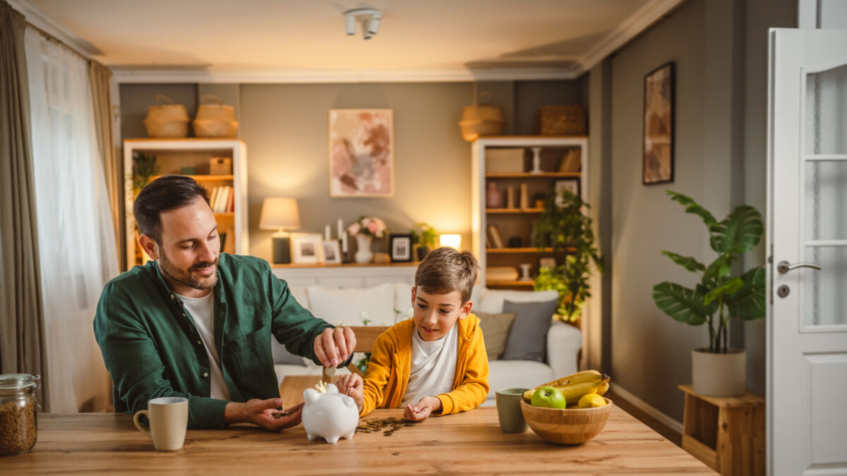 Father and son save money coins together at piggy bank at home