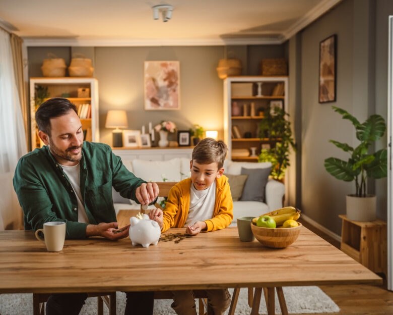 Father and son save money coins together at piggy bank at home