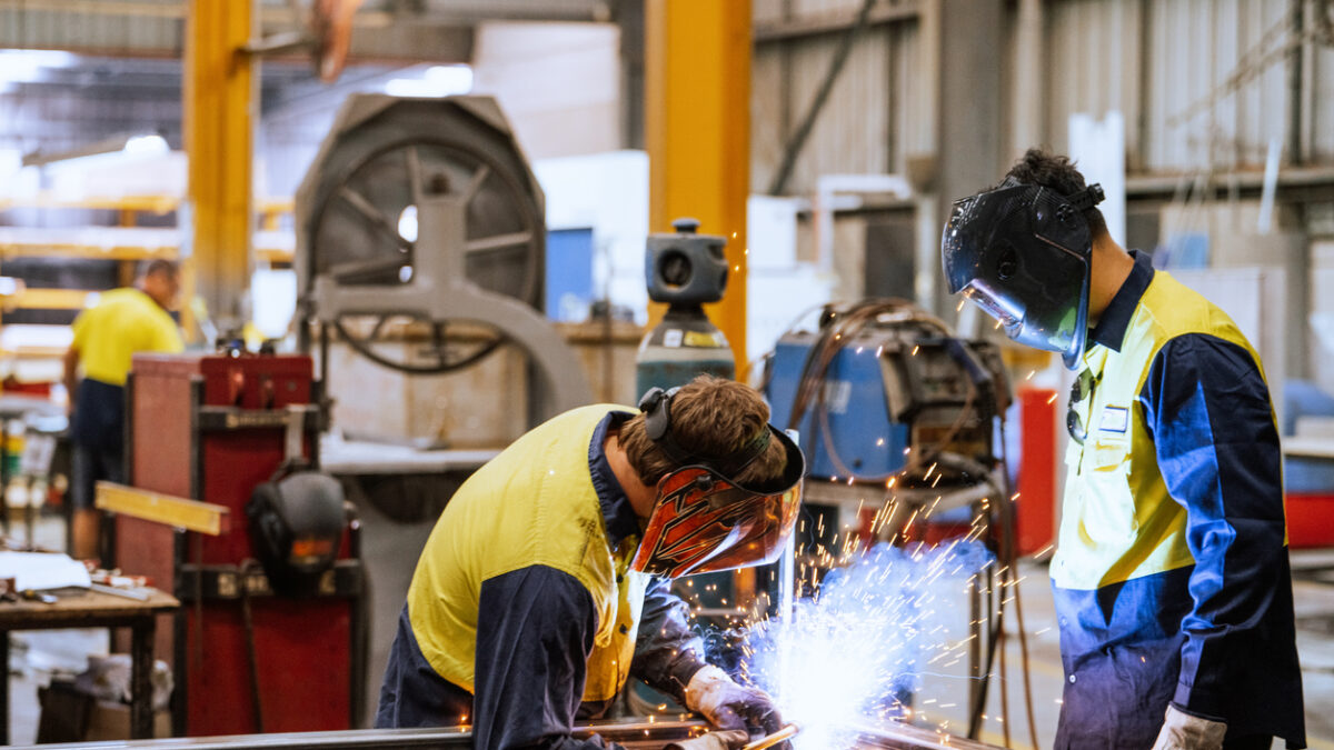 Large industrial warehouse with machinery and yellow support structures , with steel and metal processing equipment, welders welding steel bars