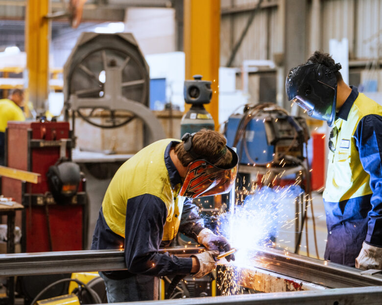 Large industrial warehouse with machinery and yellow support structures , with steel and metal processing equipment, welders welding steel bars