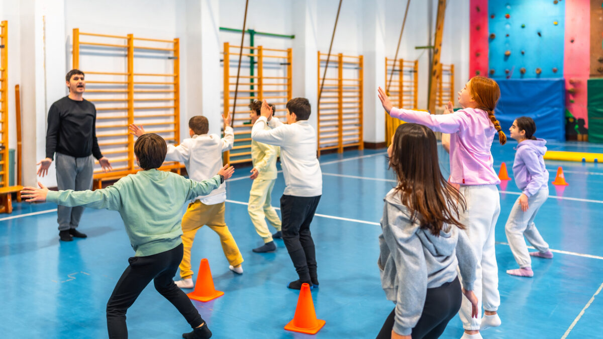 Elementary school students practicing gymnastics exercises with their teacher in the school gym