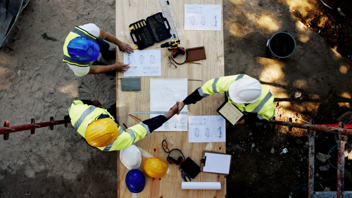Blueprint, architecture and men at table shaking hands for collaboration, agreement and inspection from above. Construction, building team and contractor on site with floor plan, handshake and deal