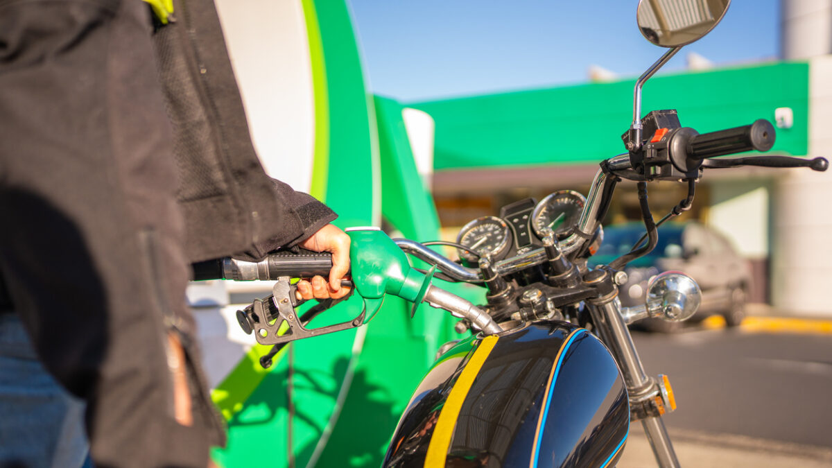 Close-up of a motorcyclist refuelling a classic motorbike at a petrol station.