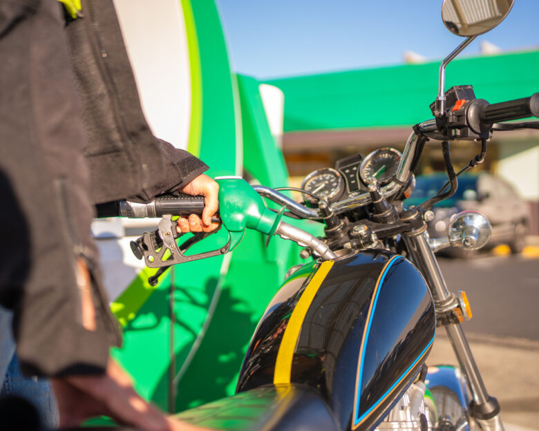 Close-up of a motorcyclist refuelling a classic motorbike at a petrol station.