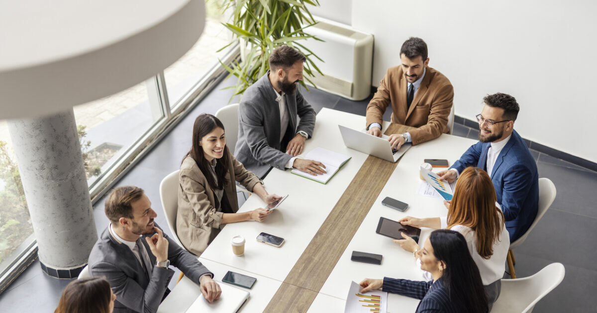 From above view of team of executives sitting at conference table at boardroom and having briefing.