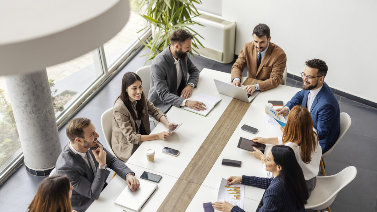 From above view of team of executives sitting at conference table at boardroom and having briefing.