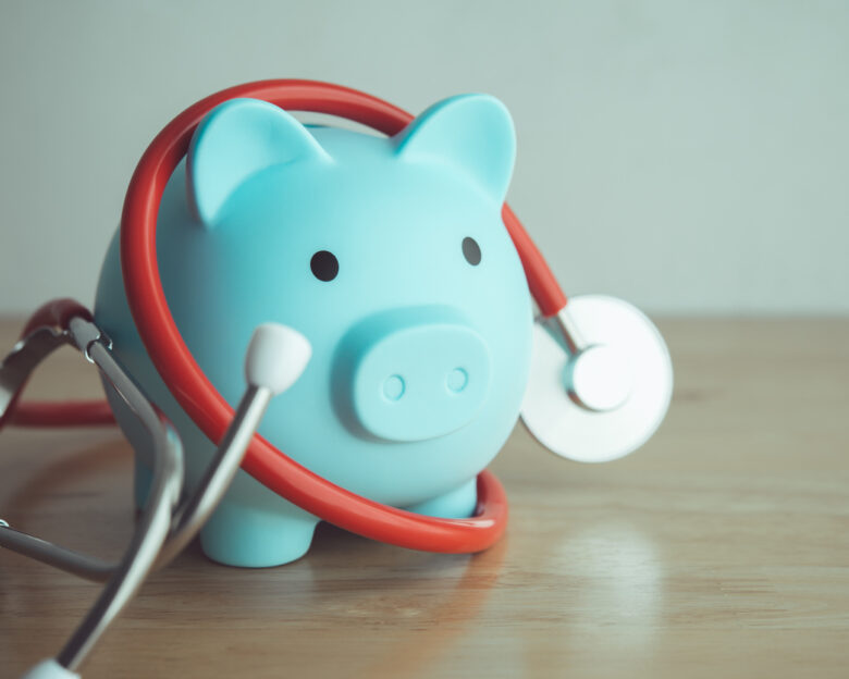 Blue piggy bank and red stethoscope on wooden table with white wall background copy space. Money savings for medical, healthcare, life insurance or personal financial checkup and so on concept.