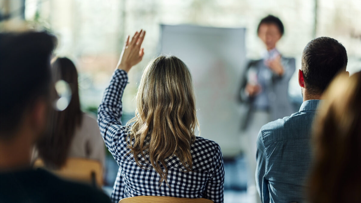Rear view of a businesswoman raising her hand to ask the question on a seminar in board room.