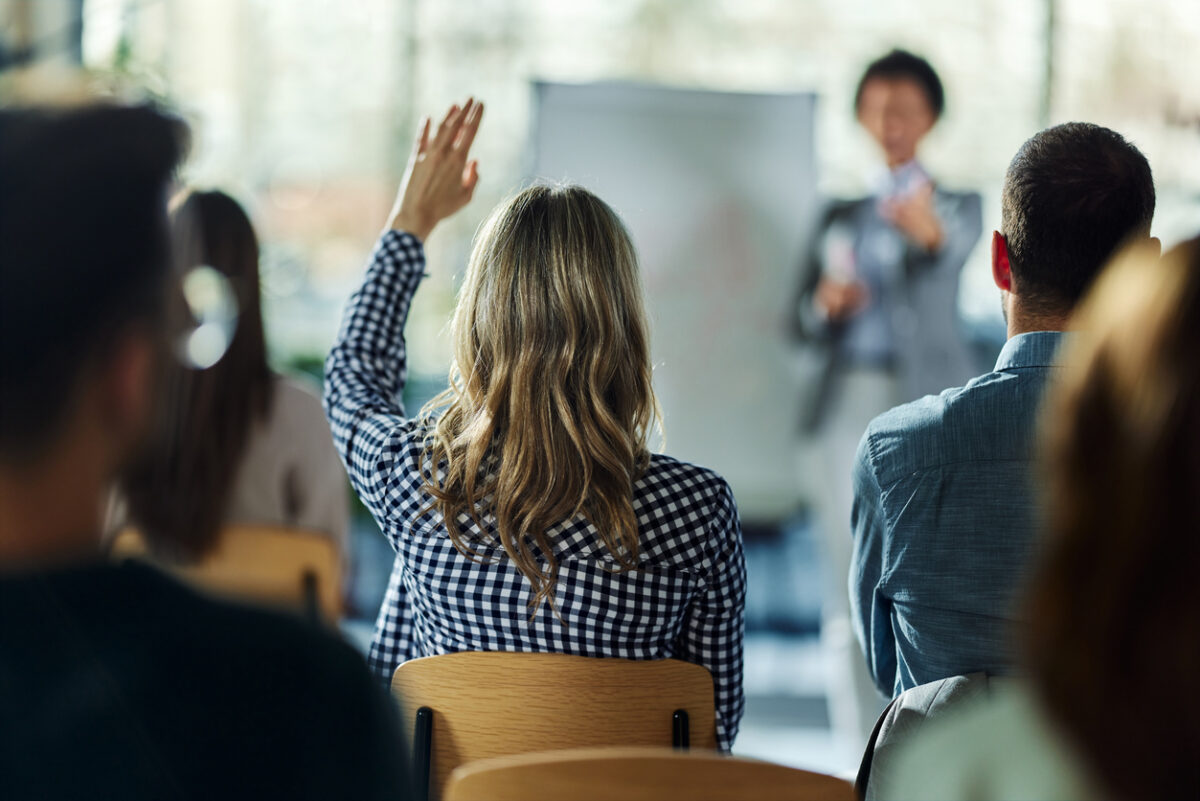 Rear view of a businesswoman raising her hand to ask the question on a seminar in board room.