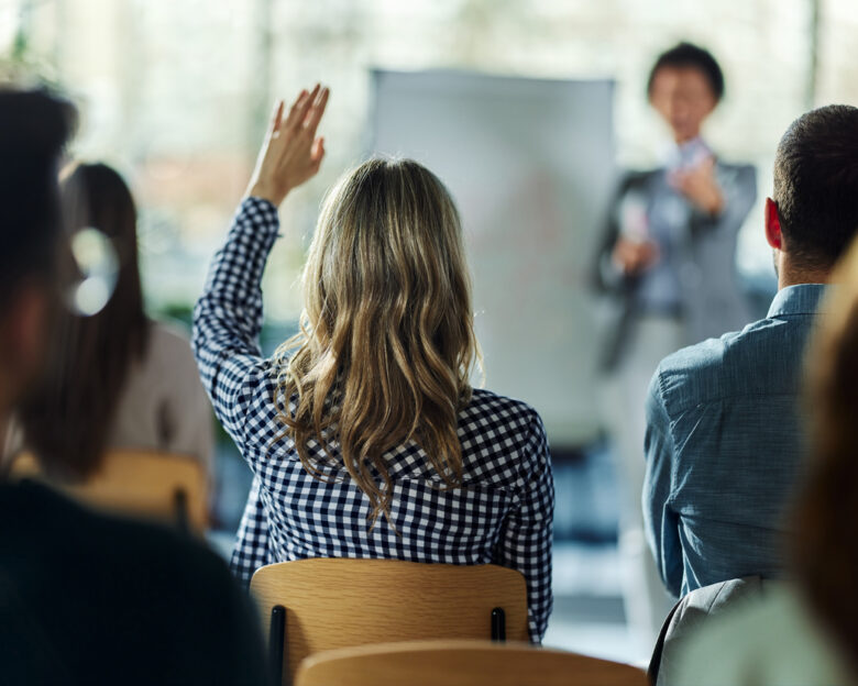 Rear view of a businesswoman raising her hand to ask the question on a seminar in board room.