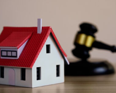 Mini house on judge’s gavel, legal book beside it “Real-estate law and property auction concept – miniature house on judge’s gavel symbolizing home ownership and legal judgement.”