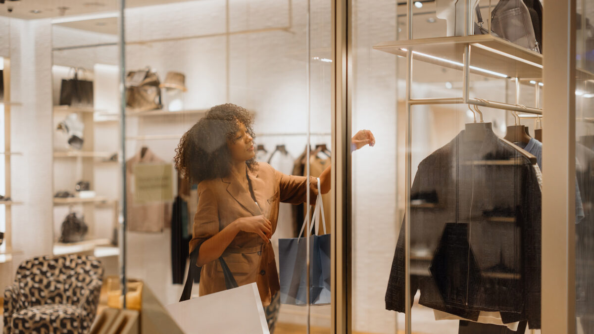 Elegant female customer looking and touching clothes in a fashion boutique, holding shopping bags