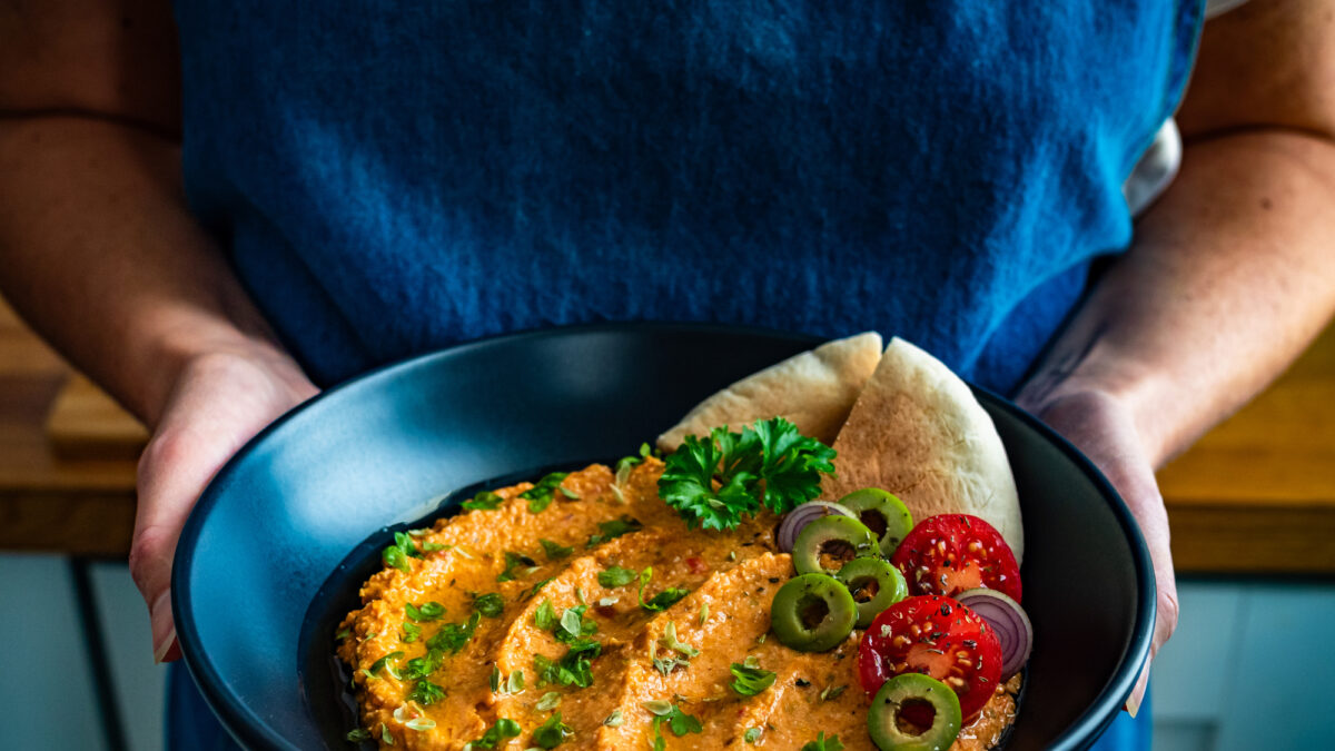 Woman chef holding bowl with whipped feta tomato dip and pita bread, close-up