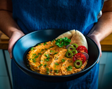 Woman chef holding bowl with whipped feta tomato dip and pita bread, close-up