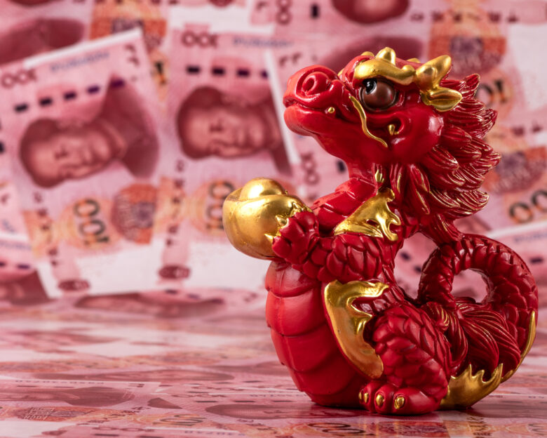A figurine of a symbolic Chinese dragon - a symbol of wisdom, strength, longevity and power, bringing good luck and prosperity against the background of 100 Chinese yuan bills.