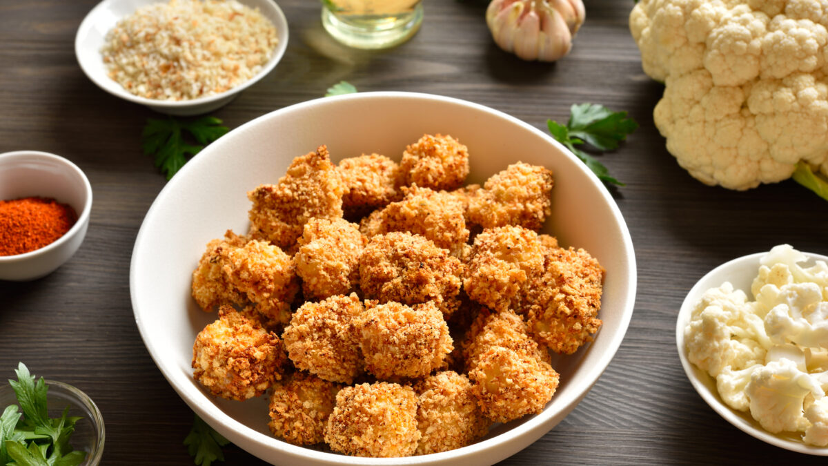 Breaded oven baked cauliflower bites in bowl on wooden table. Close up view