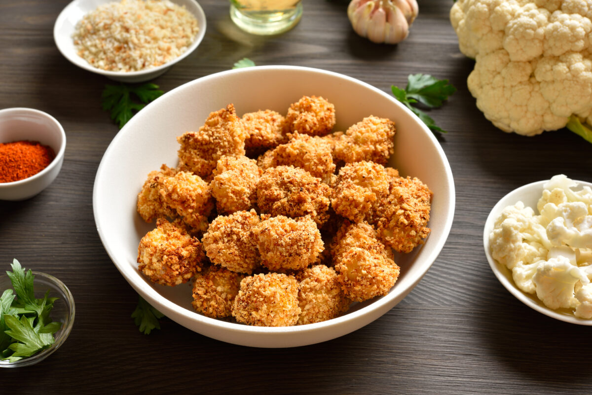 Breaded oven baked cauliflower bites in bowl on wooden table. Close up view