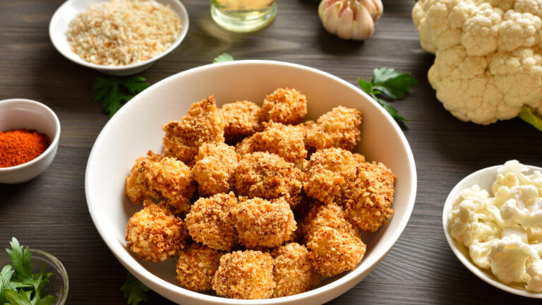 Breaded oven baked cauliflower bites in bowl on wooden table. Close up view