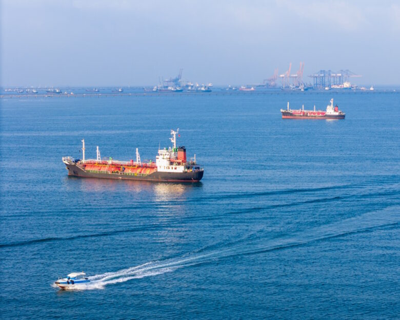 LPG gas and oil tanker ships anchored in the ocean, with a fast patrol boat in the foreground. Global energy transport, war energy crisis, and Strait of Hormuz blockade concept.