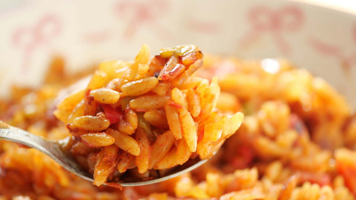 A close-up view of a spoonful of seasoned orzo with colorful vegetables.