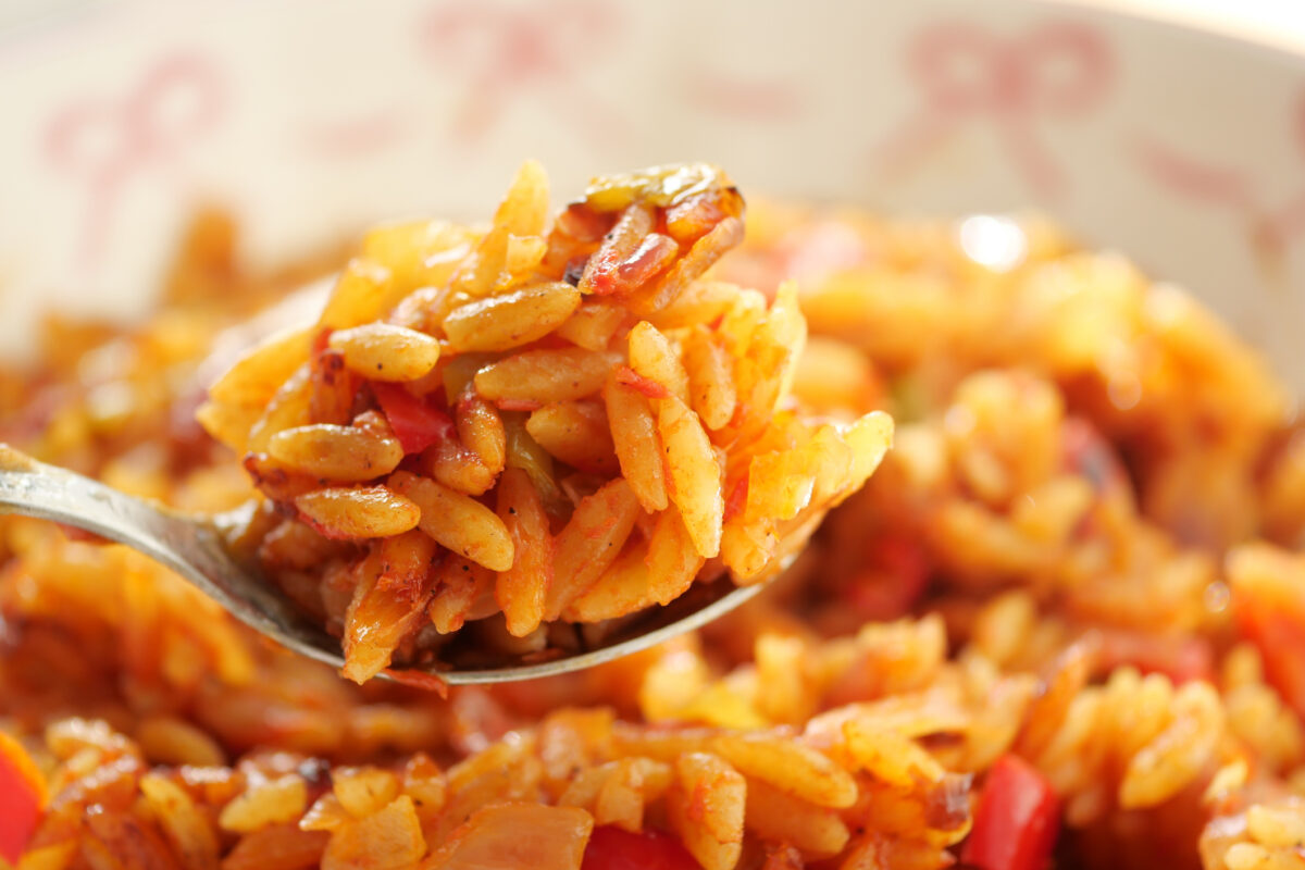 A close-up view of a spoonful of seasoned orzo with colorful vegetables.