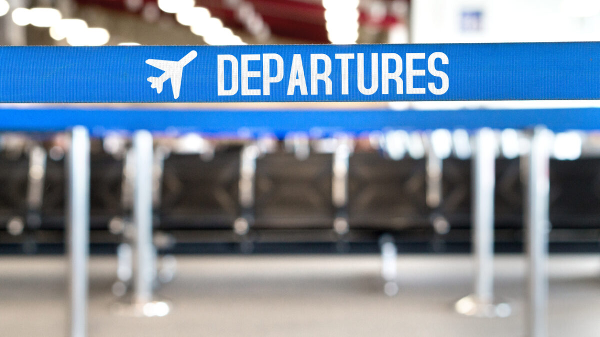 Departures text with airplane icon on a queue barrier. Waiting area and lounge seats at airport terminal.