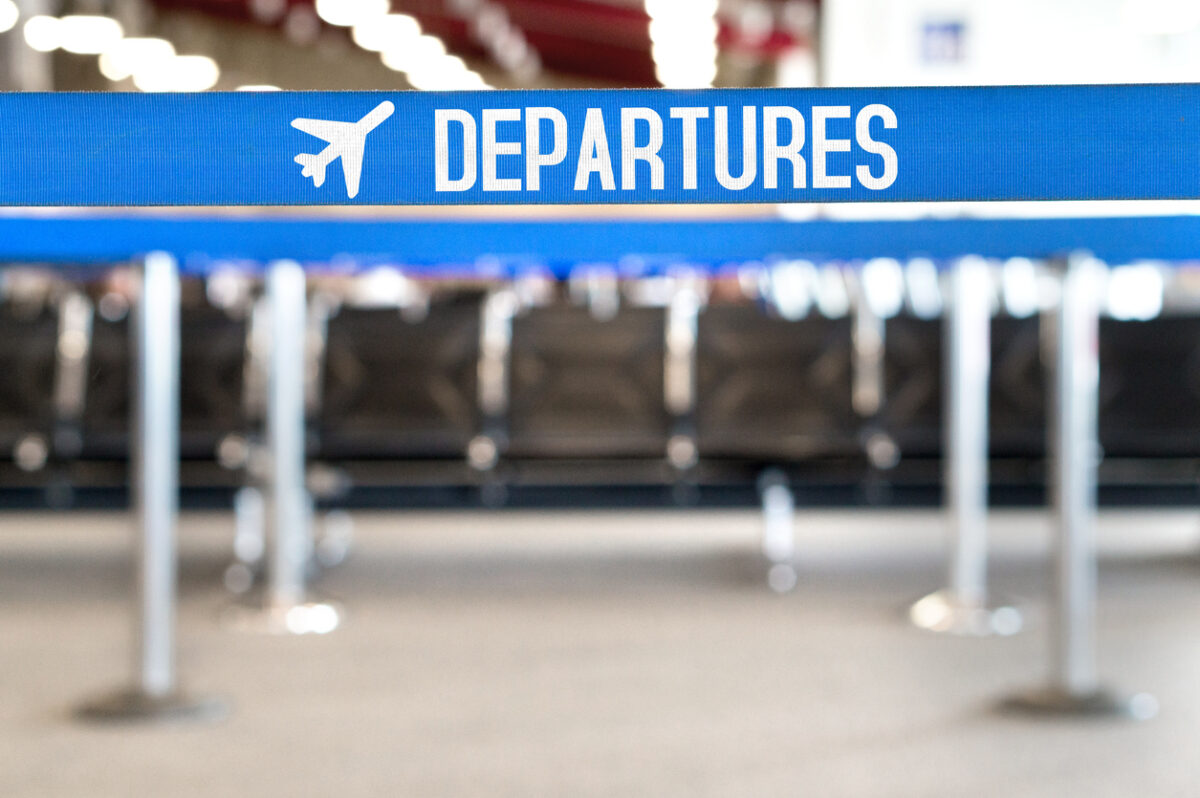 Departures text with airplane icon on a queue barrier. Waiting area and lounge seats at airport terminal.